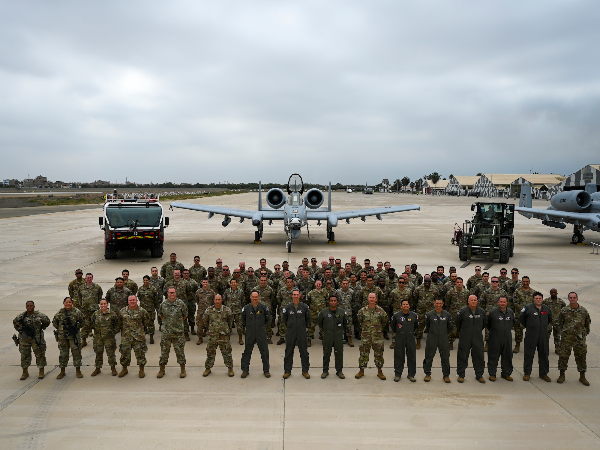 A formation of Airmen stand in front of (left to right) a fire truck, an A-10 attack aircraft, and a forklift.