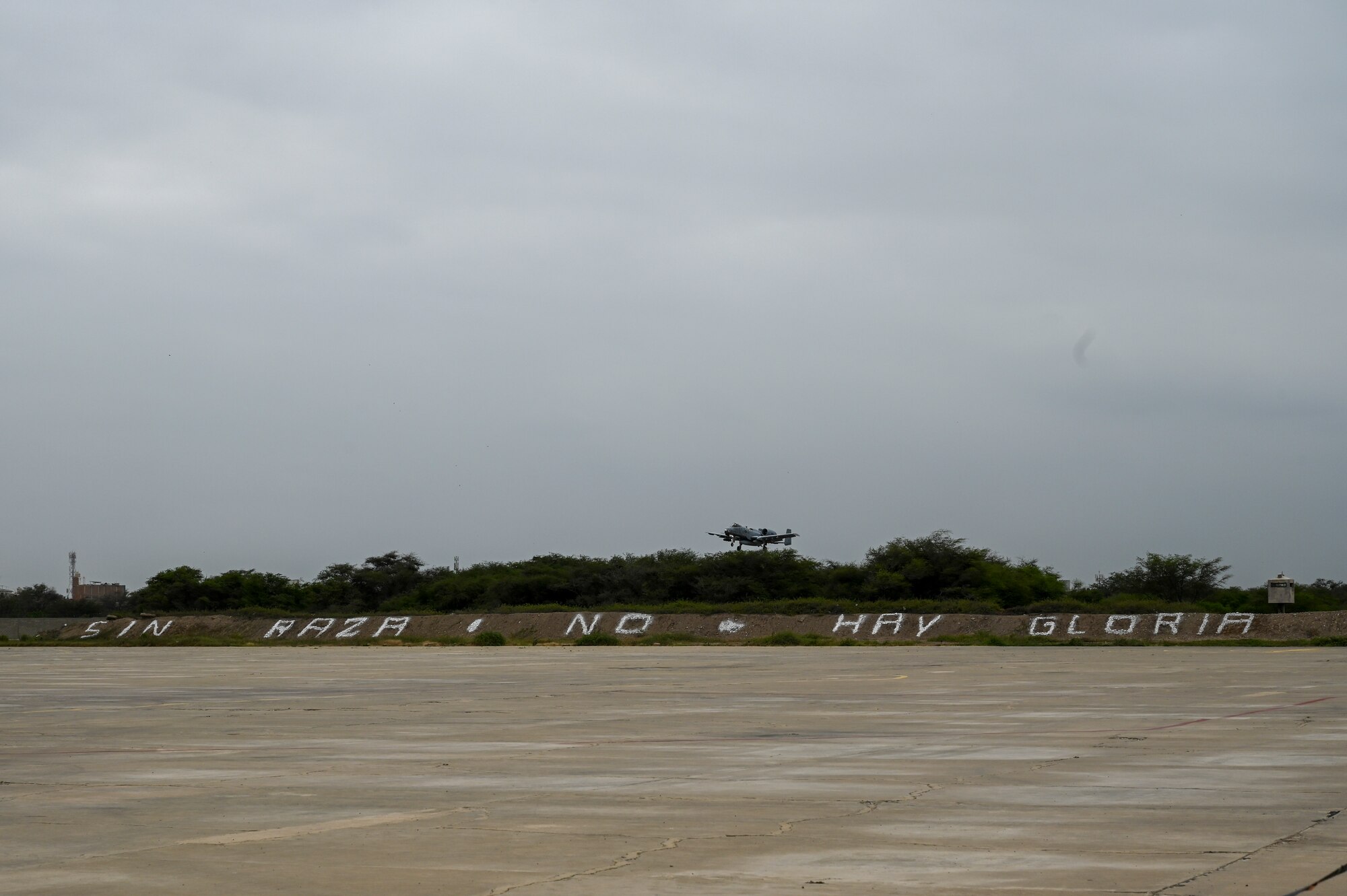 An A-10 Thunderbolt II attack aircraft comes in for landing over the motto of Fuerza Aerea del Peru's Grupo Aereo No. 6 on July 12, 2023, at Chiclayo, Peru. "Sin raza no hay gloria" is a Spanish phrase meaning "Without race, there is no glory."