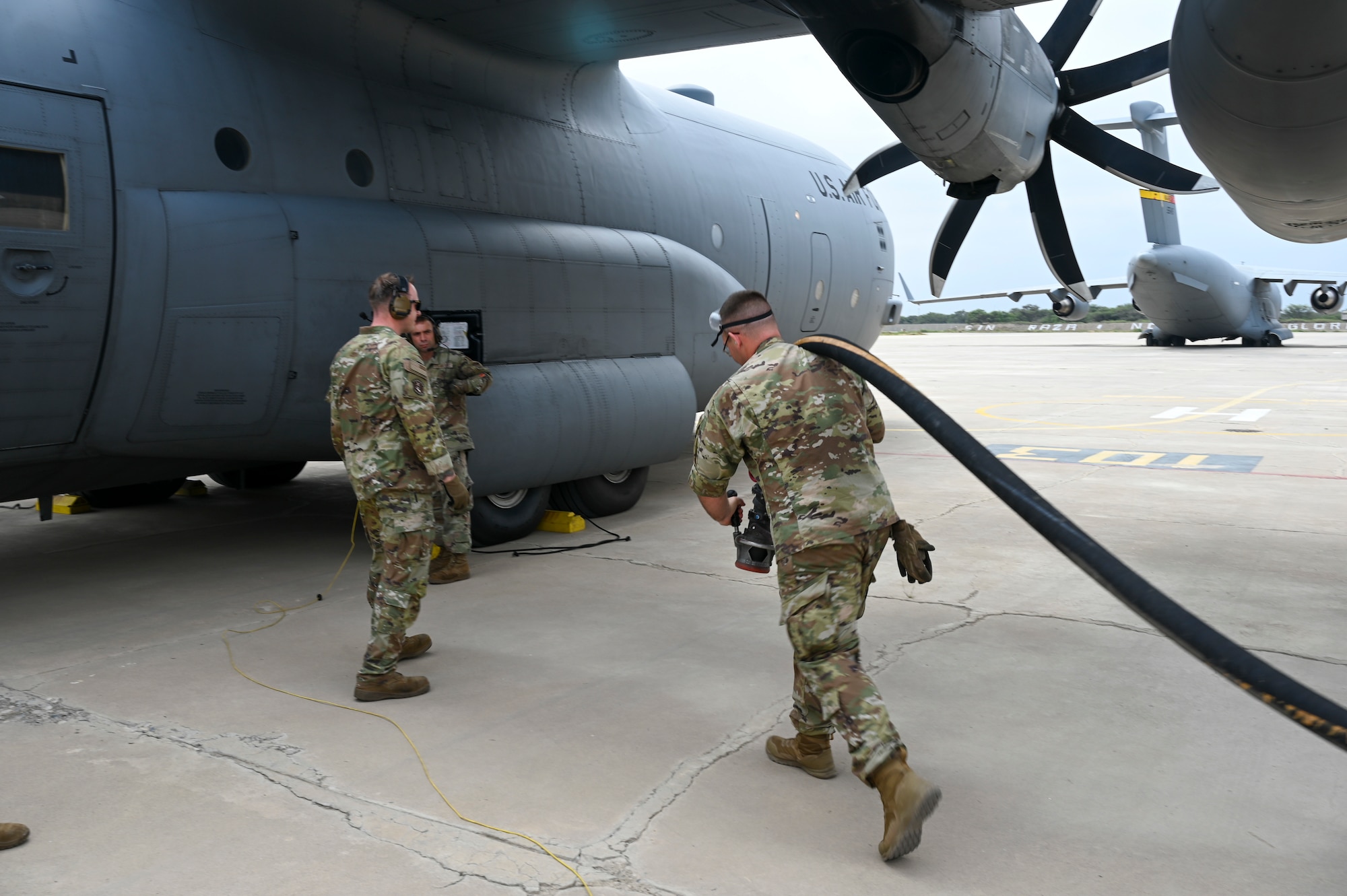 An Airman pulls a fuel hose toward a C-130 cargo aircraft while another Waits