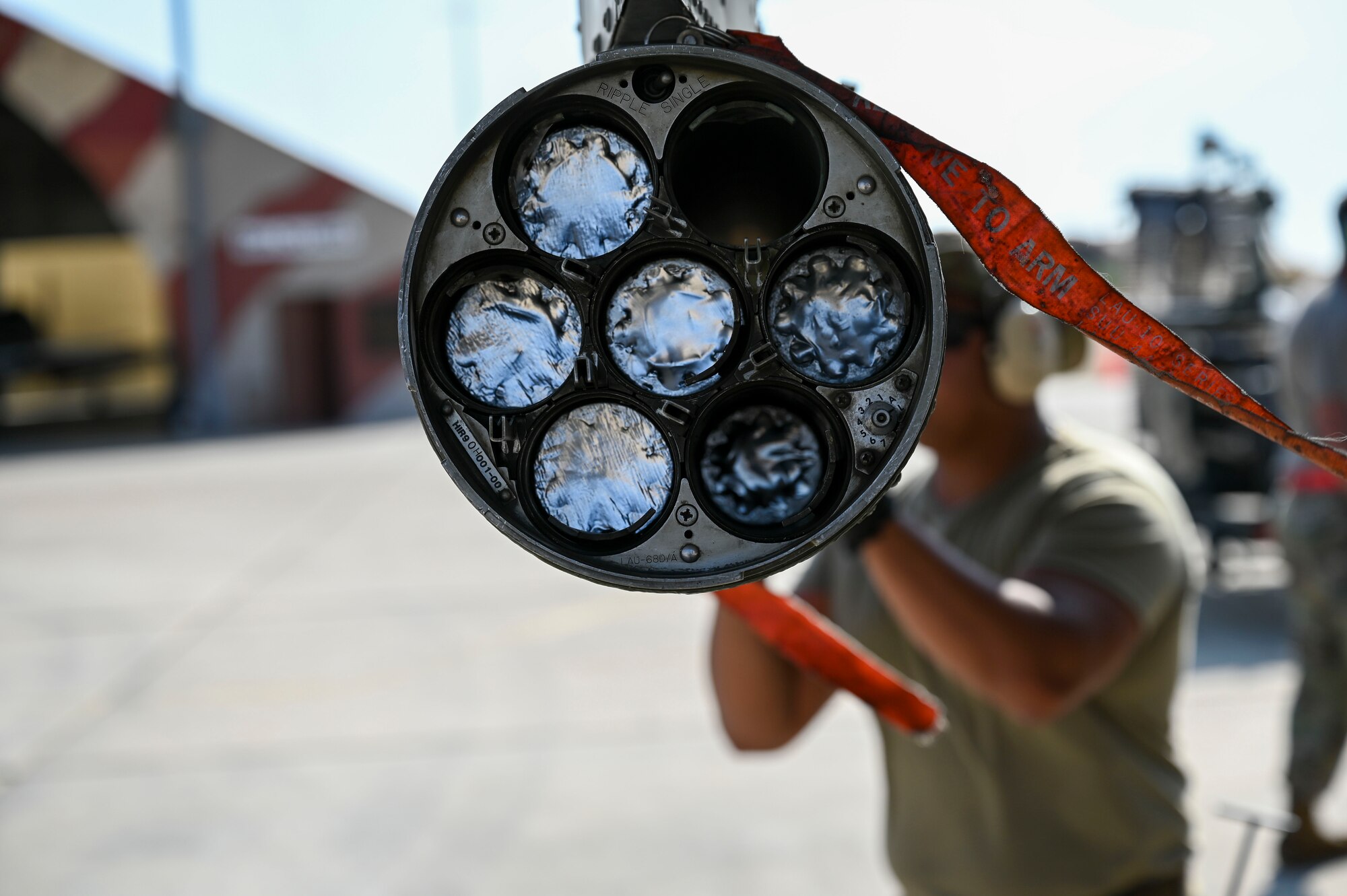 Back view of a 7-rocket tube with five rockets loaded, an empty slot, and an Airman sliding a sixth rocket into place.