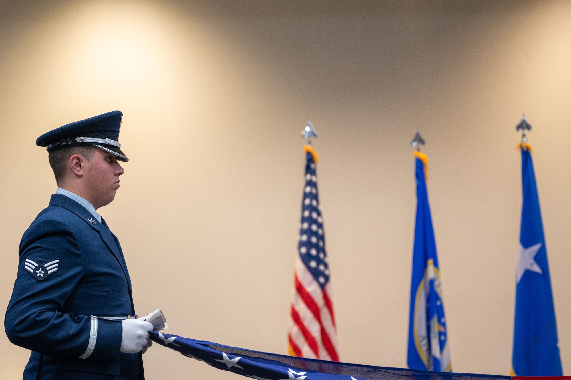 A Senior Airman in service dress holds one end of the U.S. flag during
