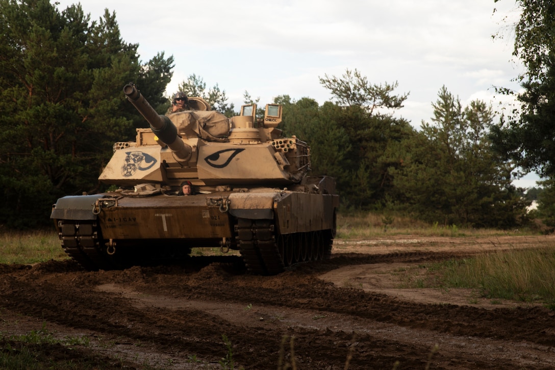 A soldier drives a tank down a road.