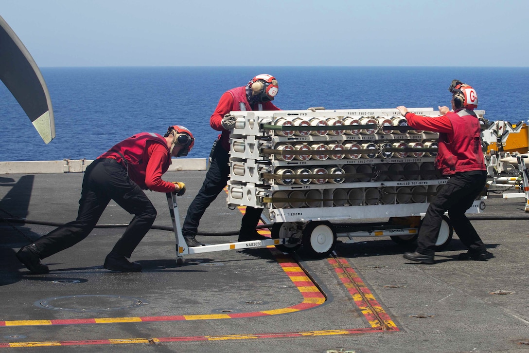 Sailors transport helicopter sonar buoys on the flight deck of a ship.