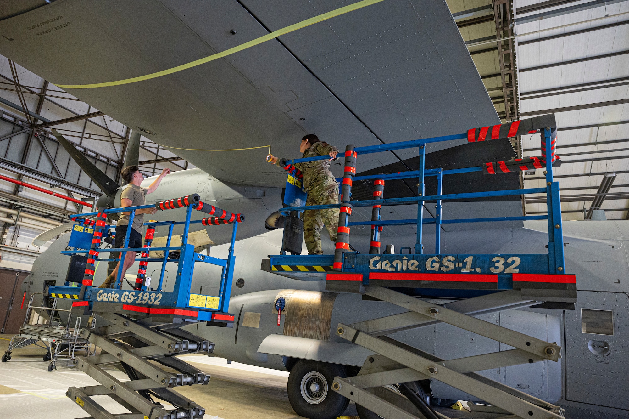 Maintenance Airmen apply tape to the wing of a C-130J Super Hercules aircraft.