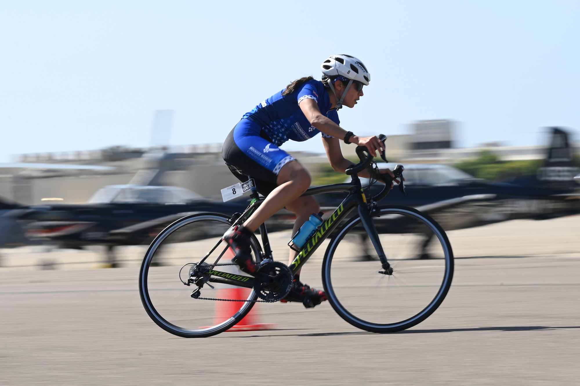 A woman rides a bicycle around a cone.