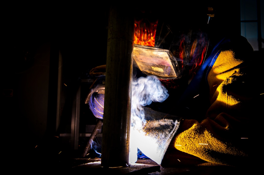 Steelworker 2nd Class Sage Charfauros, from Agana, Guam, welds a pipe to a coupon to fabricate a new fence post for the water treatment plant in the steel shop at Naval Air Station Sigonella, Aug. 4, 2023.