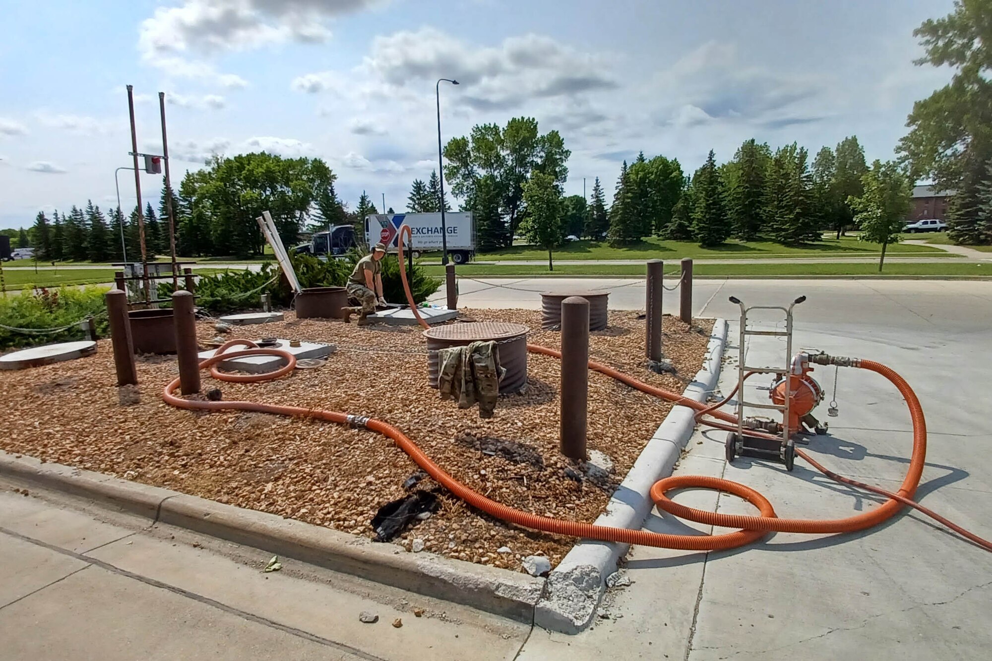 A person in a military uniform monitors a hose running into a gas tank in the ground.