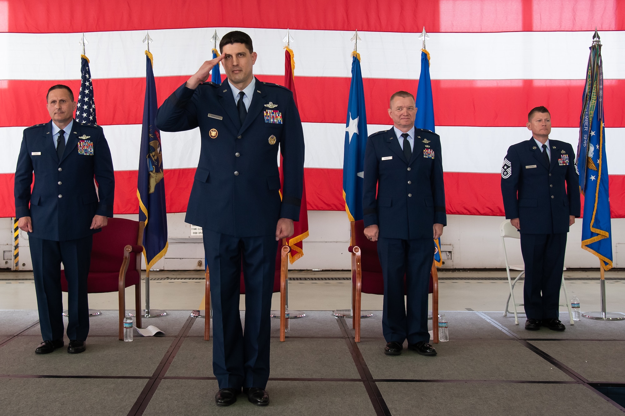 Line of four Air Force servicemembers stand at attention in a line. The second from left is saluting.