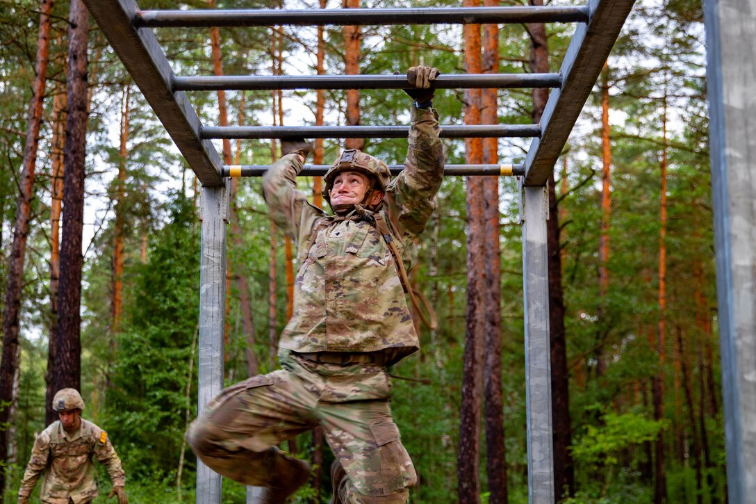 A uniformed soldier maneuvers through a horizontal ladder during an obstacle course.