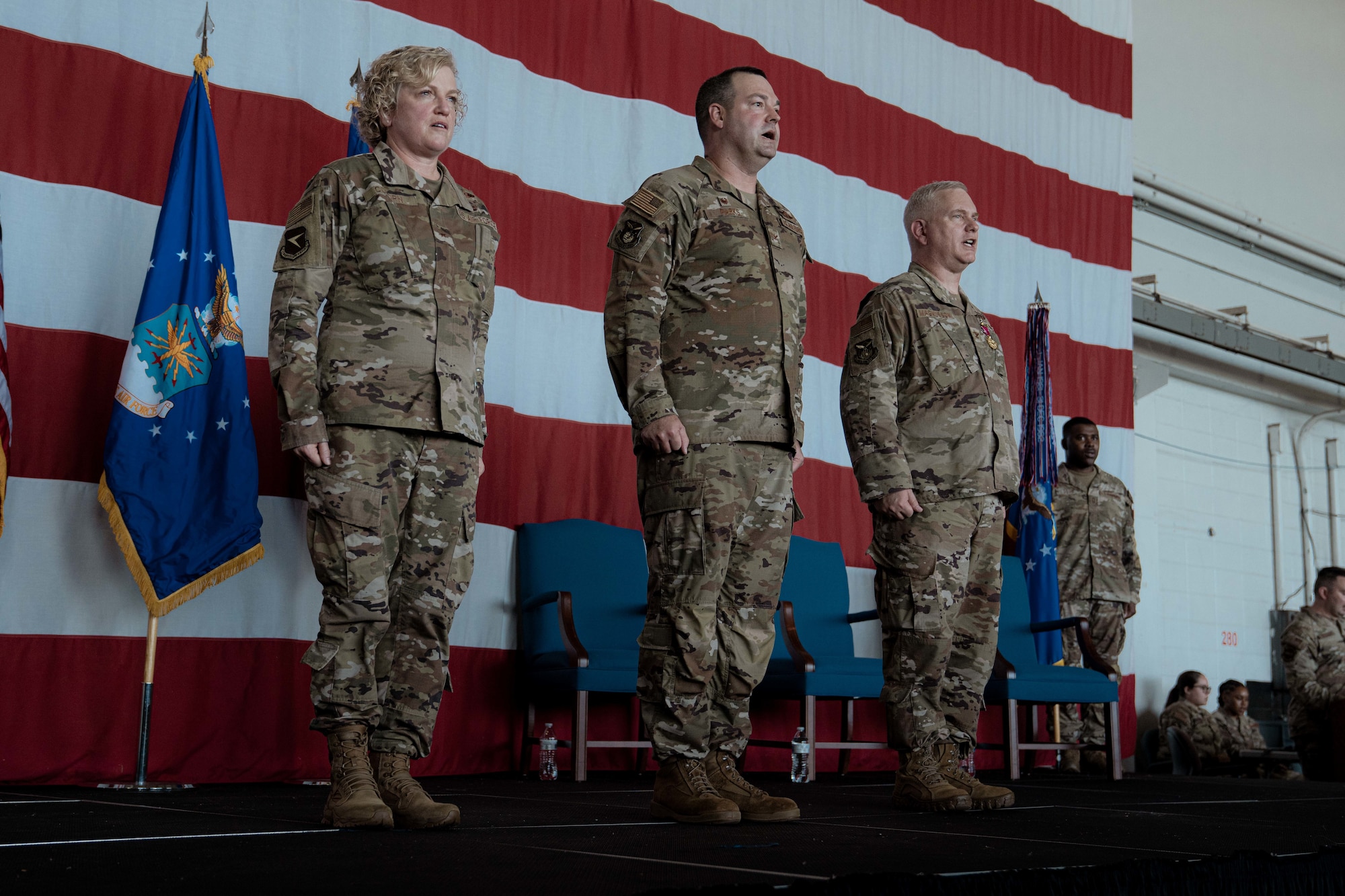 Commanders from the 22nd Air Force and 94th Airlift Wing stand at attention on stage during a change of command ceremony.