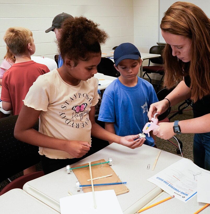 IMAGE: Stephanie Shand, a scientist in the Integrated Combat Systems Department at Naval Surface Warfare Center Dahlgren Division, uses a glue gun to help youth construct a sail car during the Spotsylvania County Sheriff’s Office STEM Camp July 31 at the Germanna Community College Fredericksburg Area Campus.