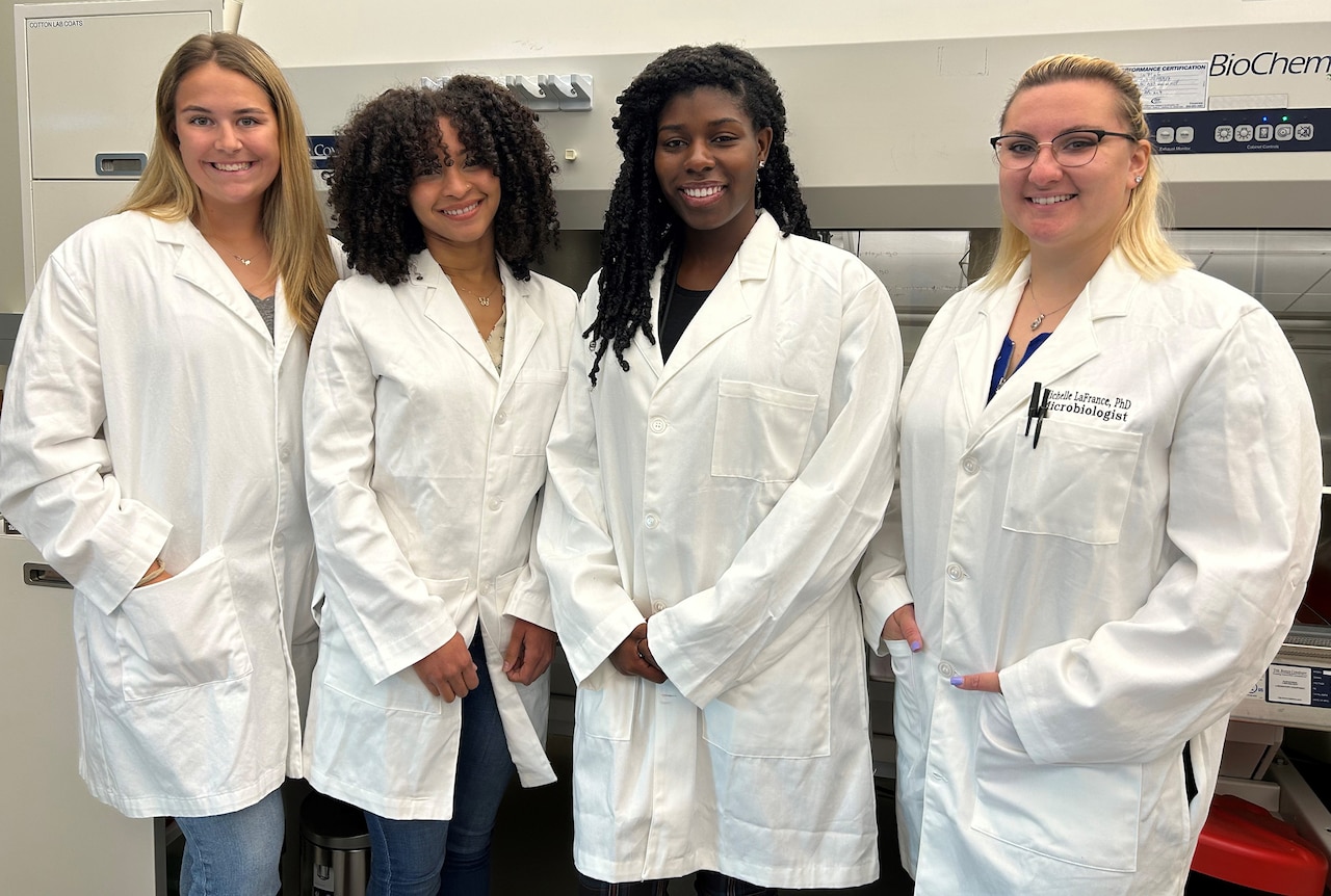 Four scientists in lab coats smile for a photo.