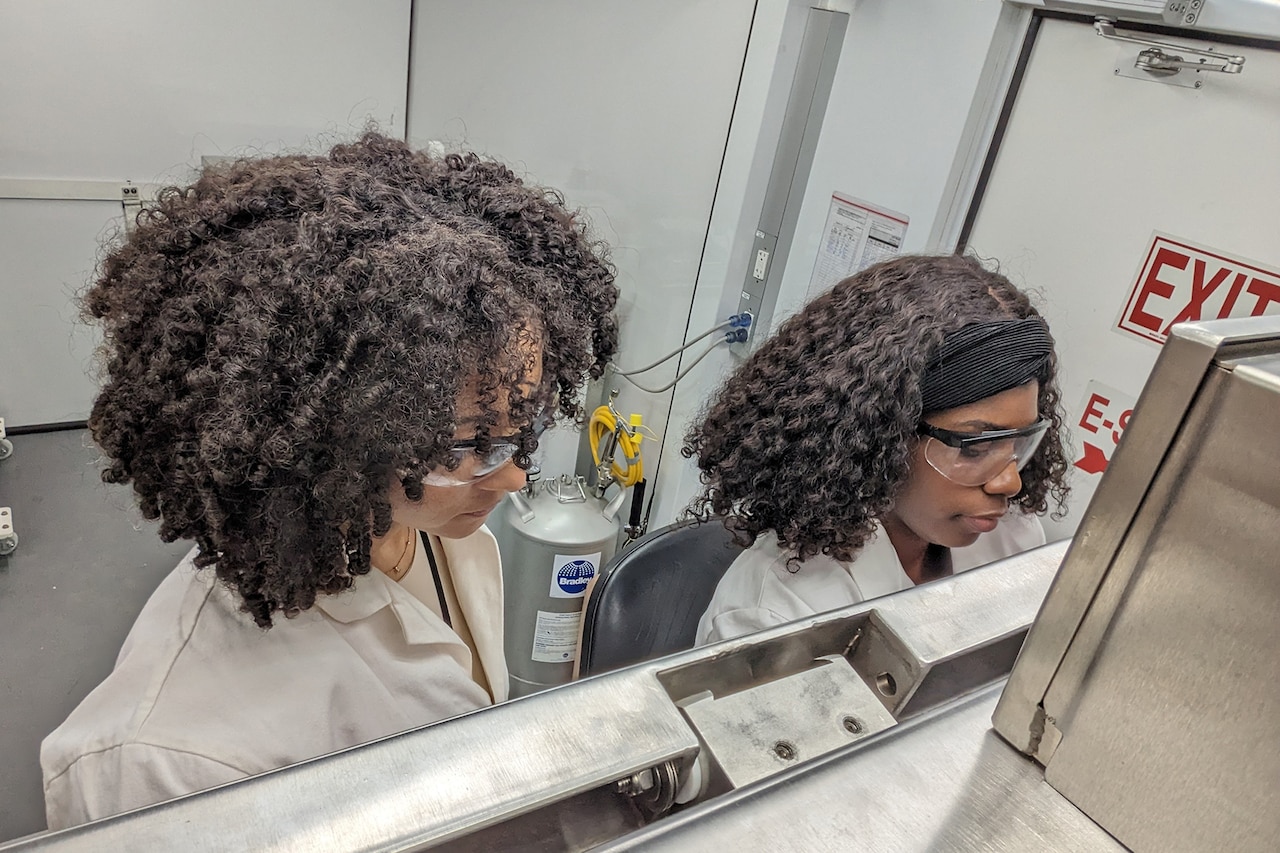 Two scientists in lab coats and protective goggles observe their work.