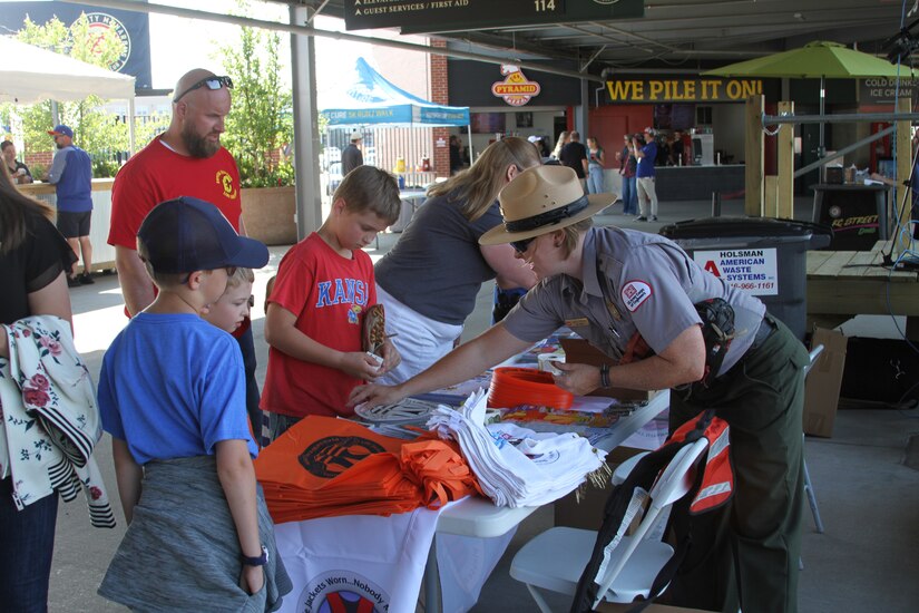 A park ranger in uniform hands out materials to two children and a man.