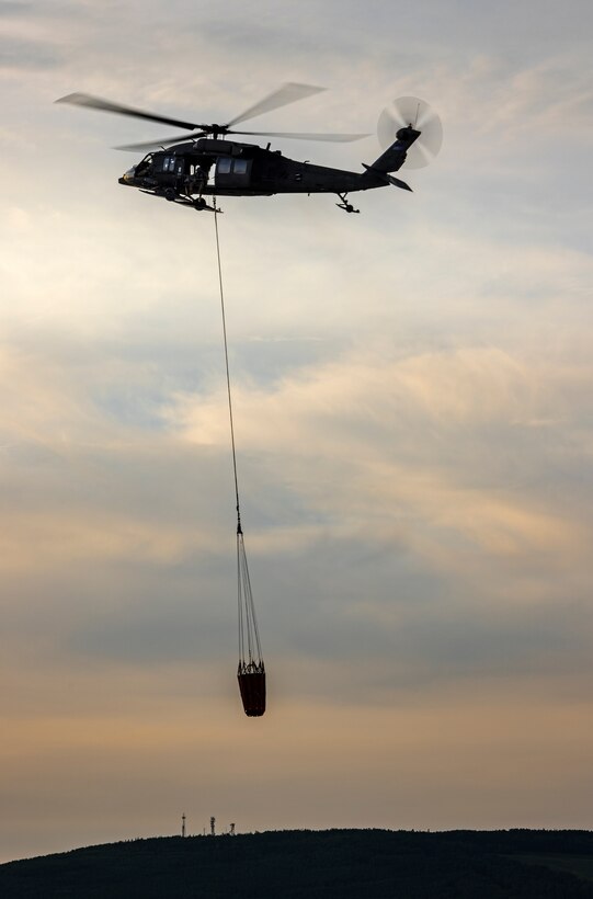 An Alaska Army National Guard UH-60L Black Hawk helicopter assigned to 207th Aviation Troop Command operates near Ladd Army Airfield Aug. 3., 2023 in support of wildland fire suppression across Interior Alaska. During fire suppression operations, the UH-60 employs a Bambi Bucket filled with approximately 630 gallons of water from a nearby lake. The Alaska Army National Guard deployed the UH-60 and air crew July 31, 2023 after receiving a resource request from the Alaska Division of Forestry and Fire Protection routed through the State Emergency Operations Center.