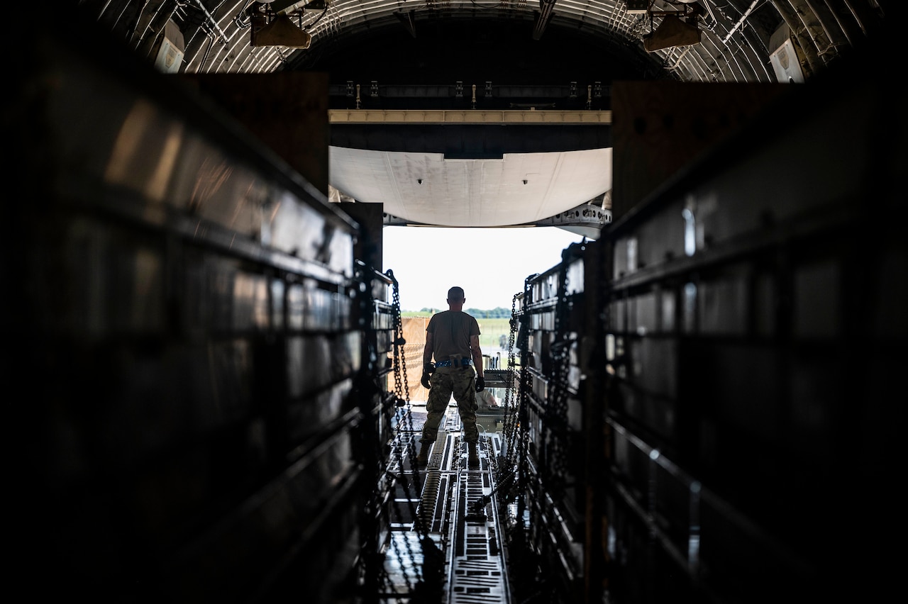 A service member stands inside a military cargo plane as weapons are loaded.