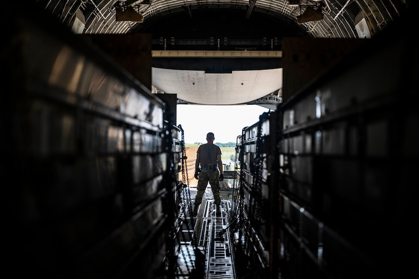 A service member stands inside a military cargo plane as weapons are loaded.