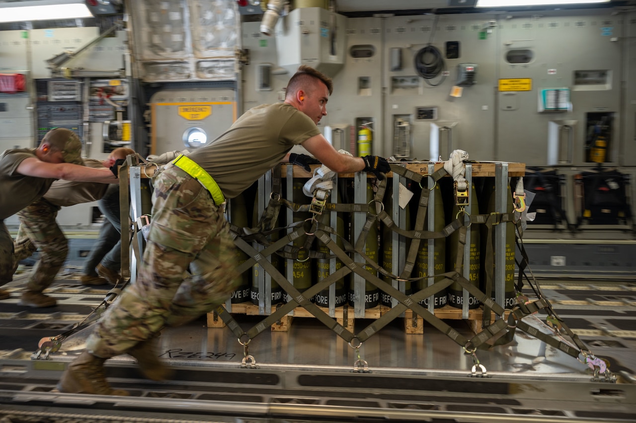 Men in uniform push a pallet of equipment into place onboard a military cargo plane.