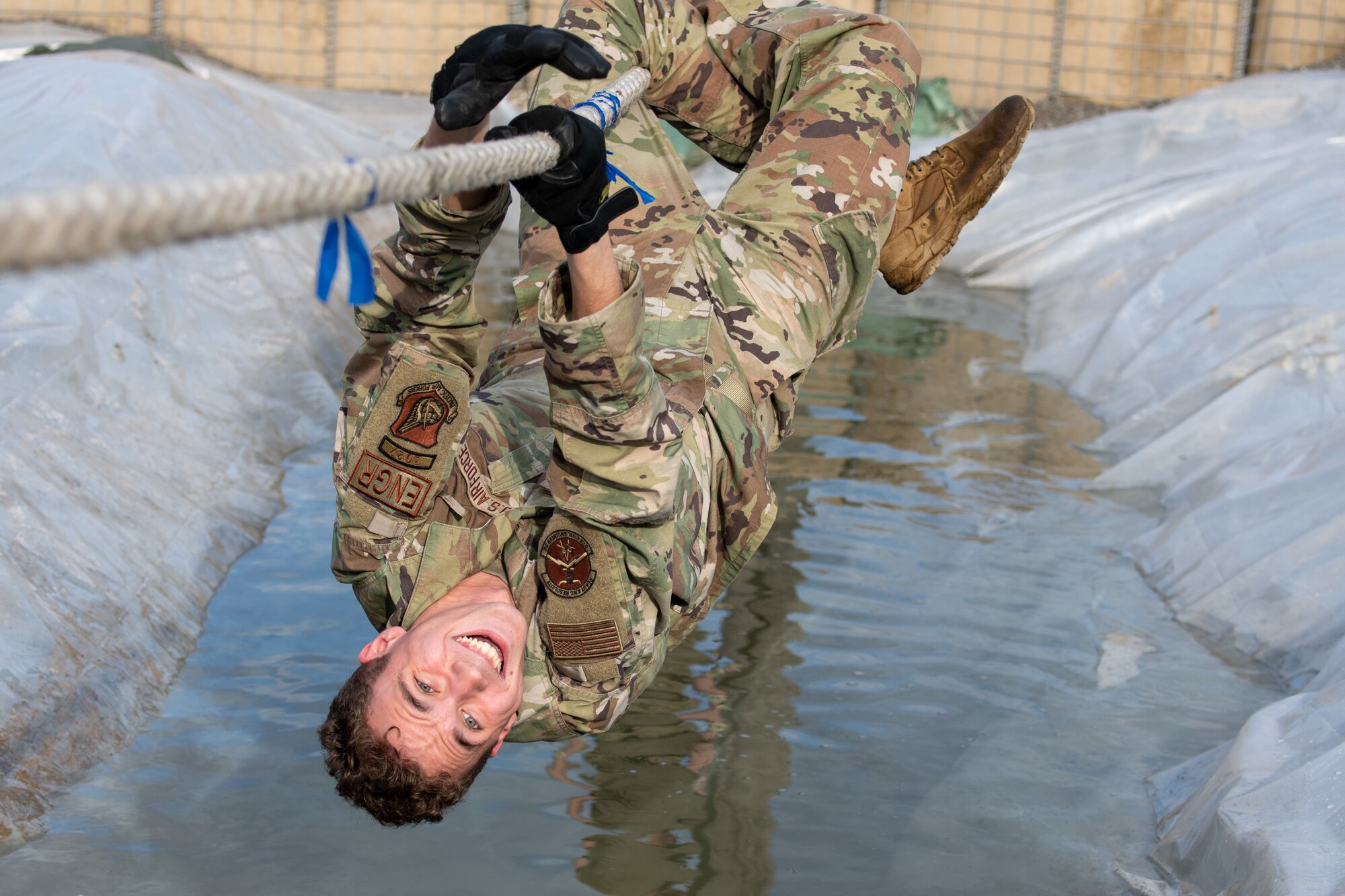 A photo of an Airman climbing across a rope bridge