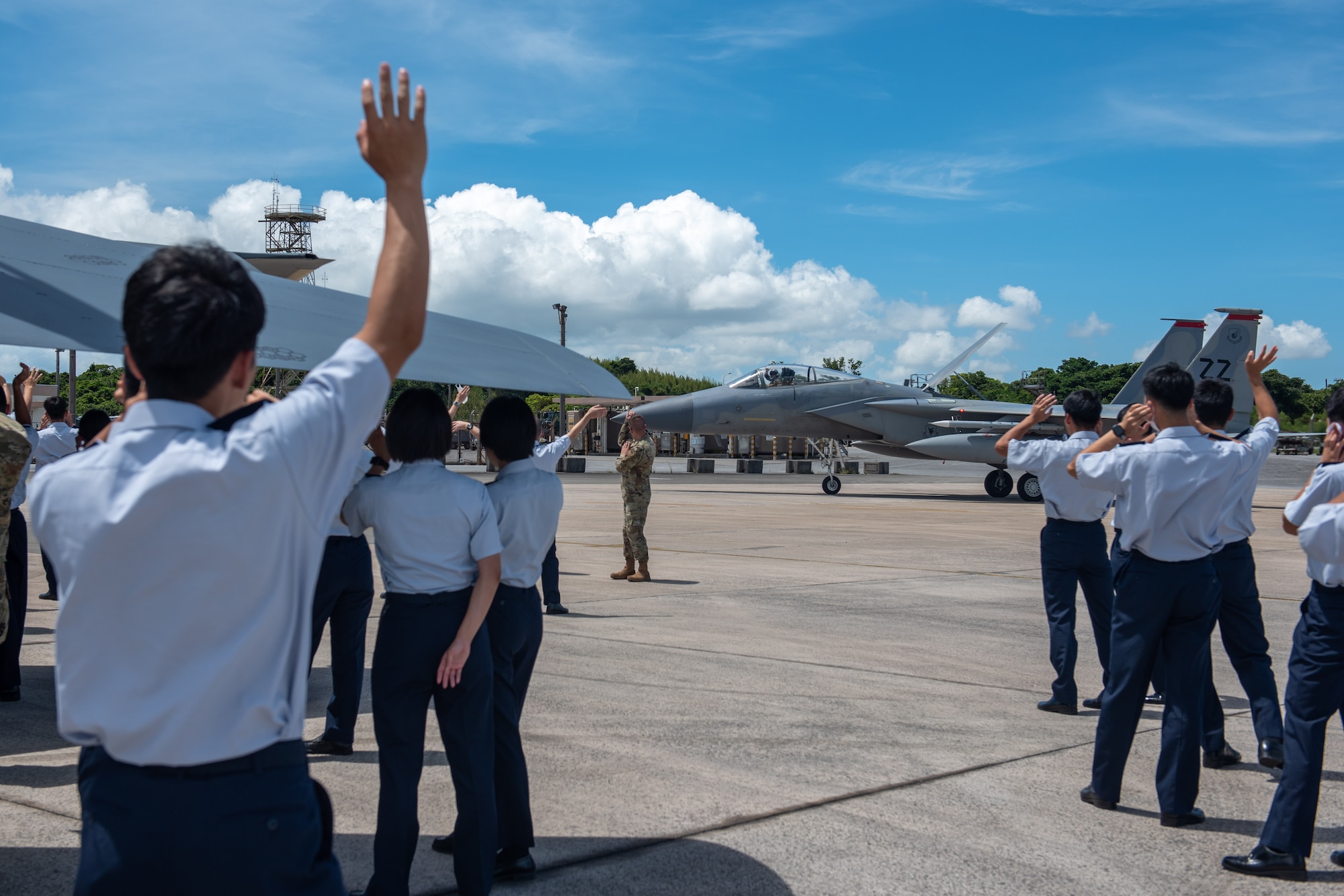 Japan Air Self-Defense Force cadets and U.S. Air Force Airmen wave at a taxiing F-15C pilot