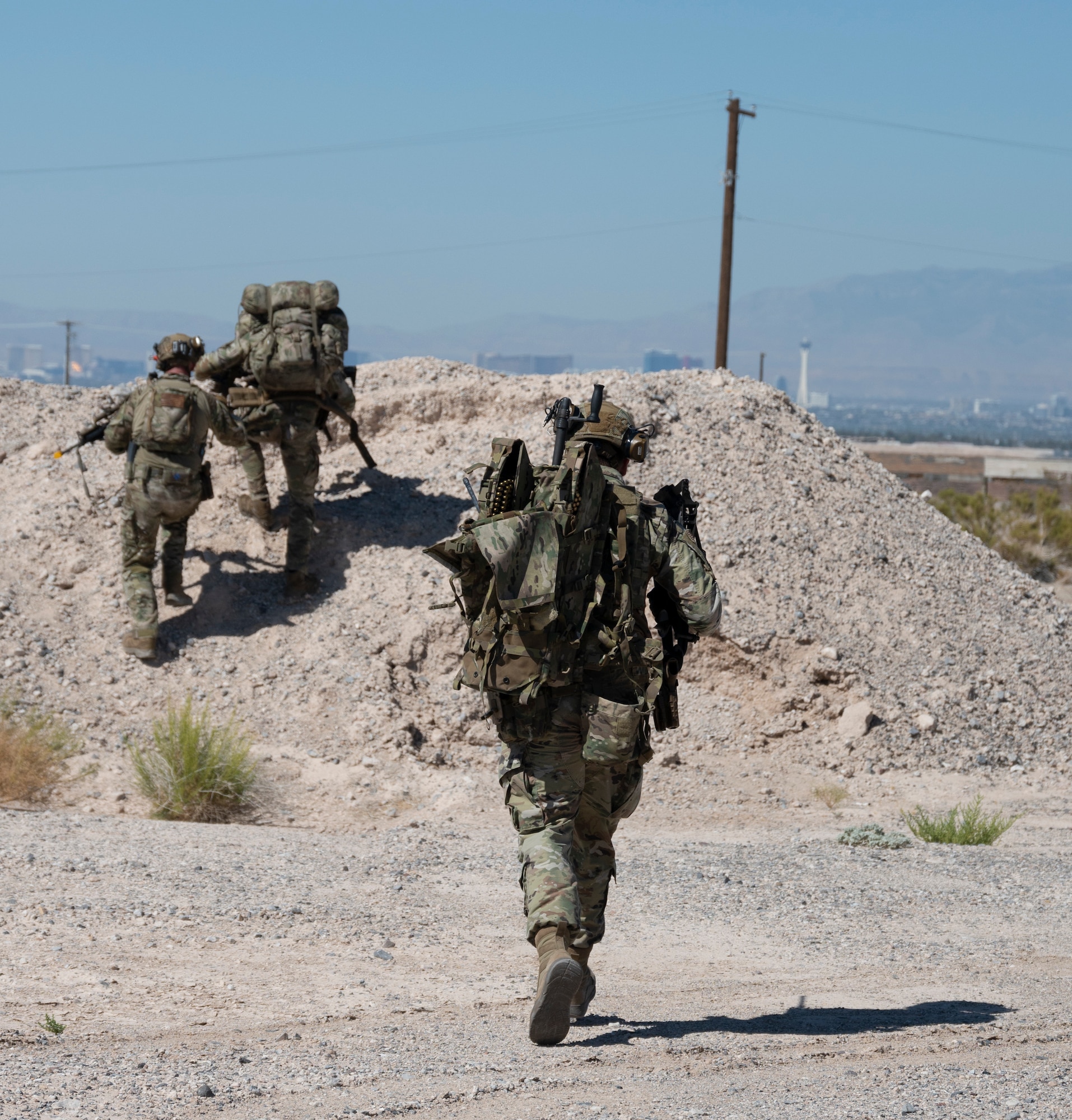 Three U.S. Airmen run toward a berm during an air base defense rehearsal during exercise Red Flag 23-3 at Nellis AFB, Nevada, July 20, 2023. These defenders were establishing security for the forward operating site and contingency locations necessary to perform Agile Combat Employment. (U.S. Air Force photo by Master Sgt. Niles Bartram)