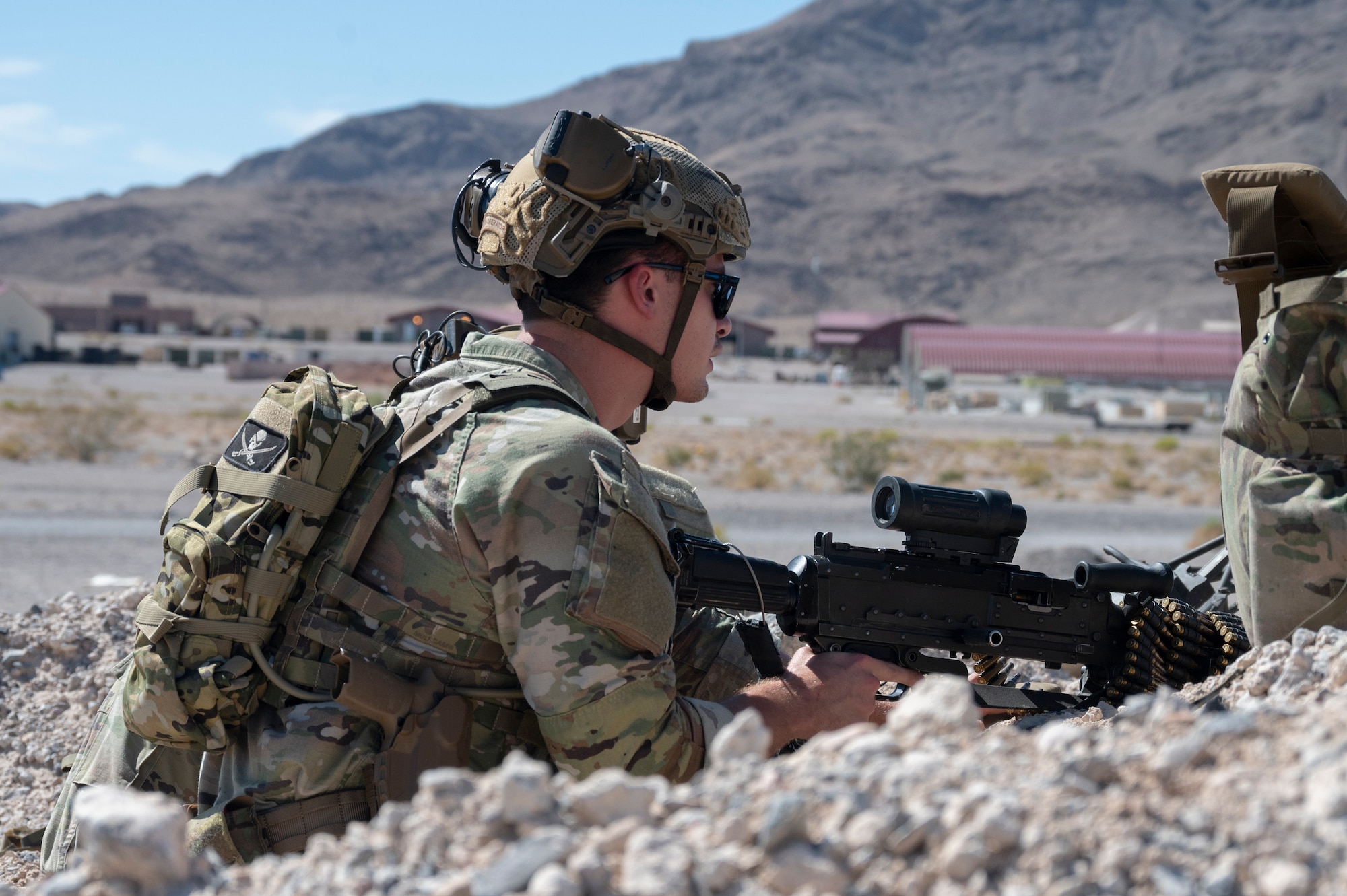 A U.S. Airman sits in a defensive fighting position armed with a light machine gun during an air base defense rehearsal during exercise Red Flag 23-3 at Nellis AFB, Nevada, July 20, 2023. These defenders were establishing security for the forward operating site and contingency locations necessary to perform Agile Combat Employment. (U.S. Air Force photo by Master Sgt. Niles Bartram)