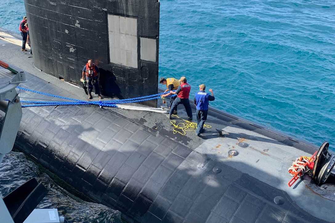 Sailors work on the top of a submarine.