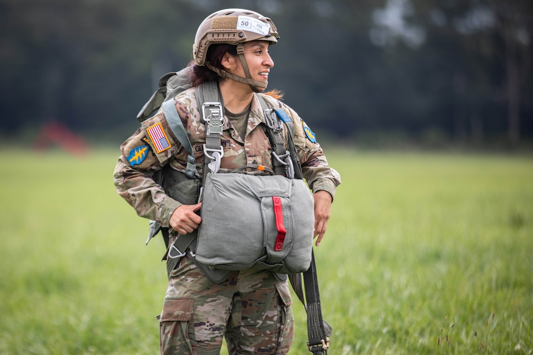 A soldier stands in a field and smiles.