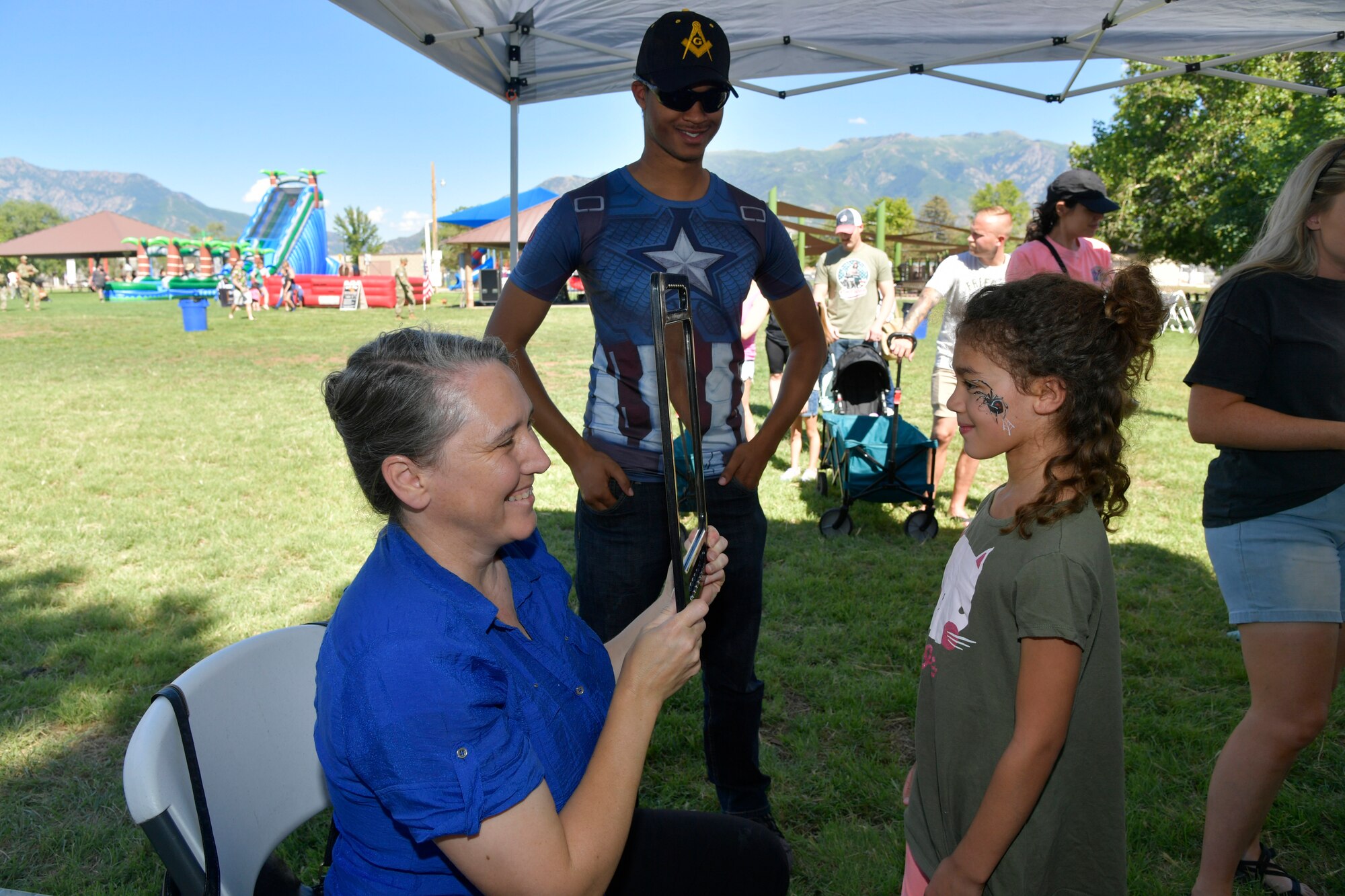 A child with her face painted looks at herself in a hand mirror.