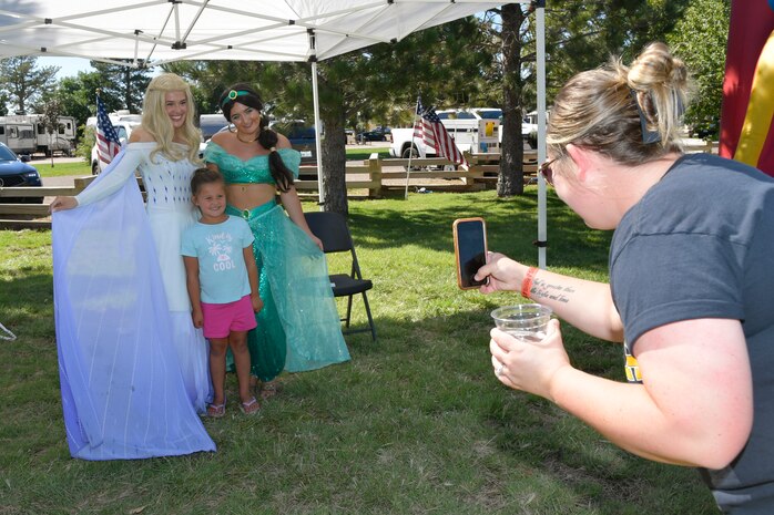 A mom takes a picture of her daughter posing with two princesses.