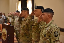 Three male soldiers saluting the flag during a change of command ceremony.