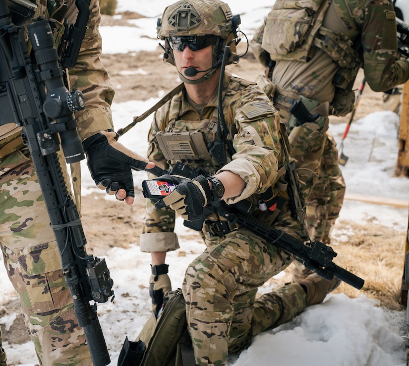 Service member kneels in the snow and reaches for small medical device that is a loaded autoinjector