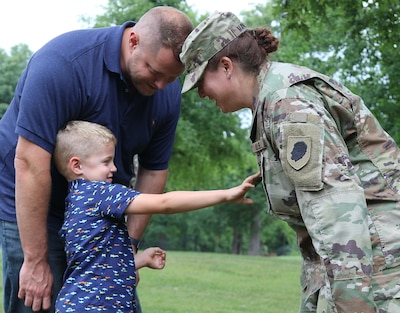Five-year-old George Steven rips the major rank from his mother's uniform during Lt. Col. Jaime Marlock's promotion ceremony. His father and her spouse, George Marlock, looks on.