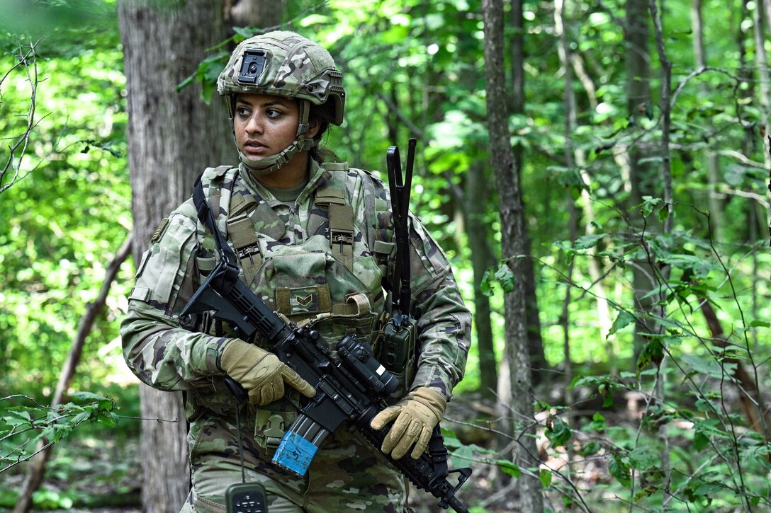 A uniformed airman holds a weapon while in a wooded area.