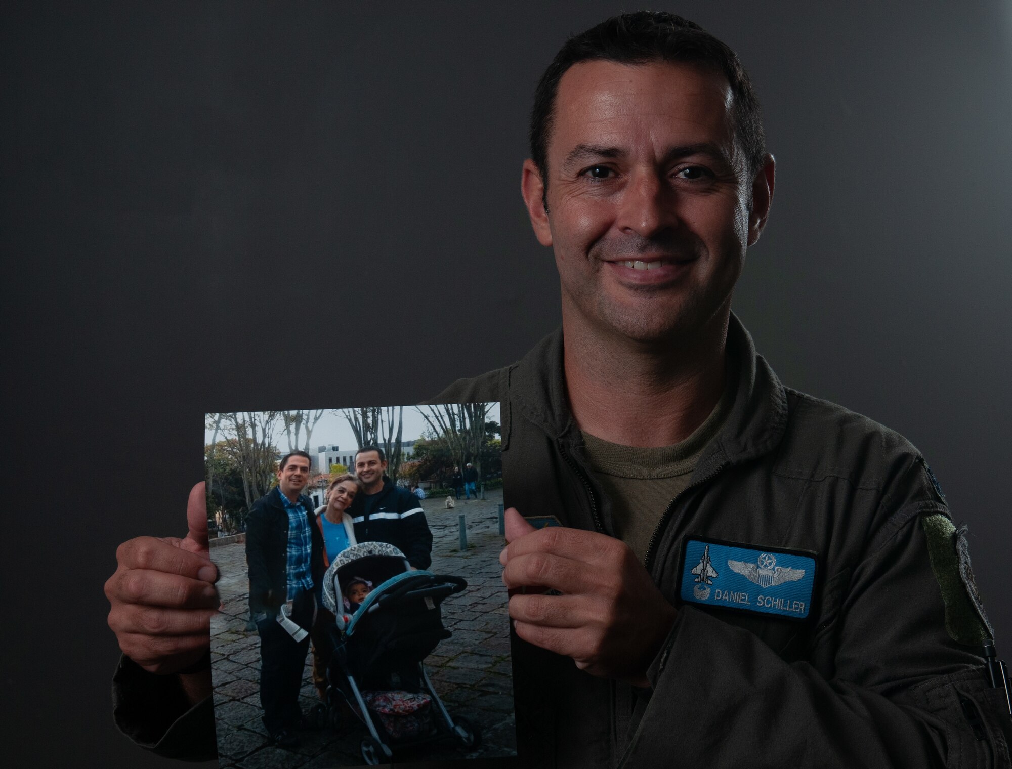 U.S. Air Force Lt. Col. Daniel Schiller, chief of safety and F-15C Eagle pilot at the 125th Fighter Wing, poses with a photo of his biological mother and brother, both from Colombia, at the Jacksonville Air National Guard Base, FL, July 31, 2023. Schiller was adopted by a U.S. couple at a young age and eventually commissioned into the Air Force in 2003. In 2018, he met his birth mother and half-brother for the first time, and in 2023, he will return to Colombia to complete his final tour of duty with the Florida Air National Guard. (U.S. Air National Guard photo by Tech Sgt. Chelsea Smith)