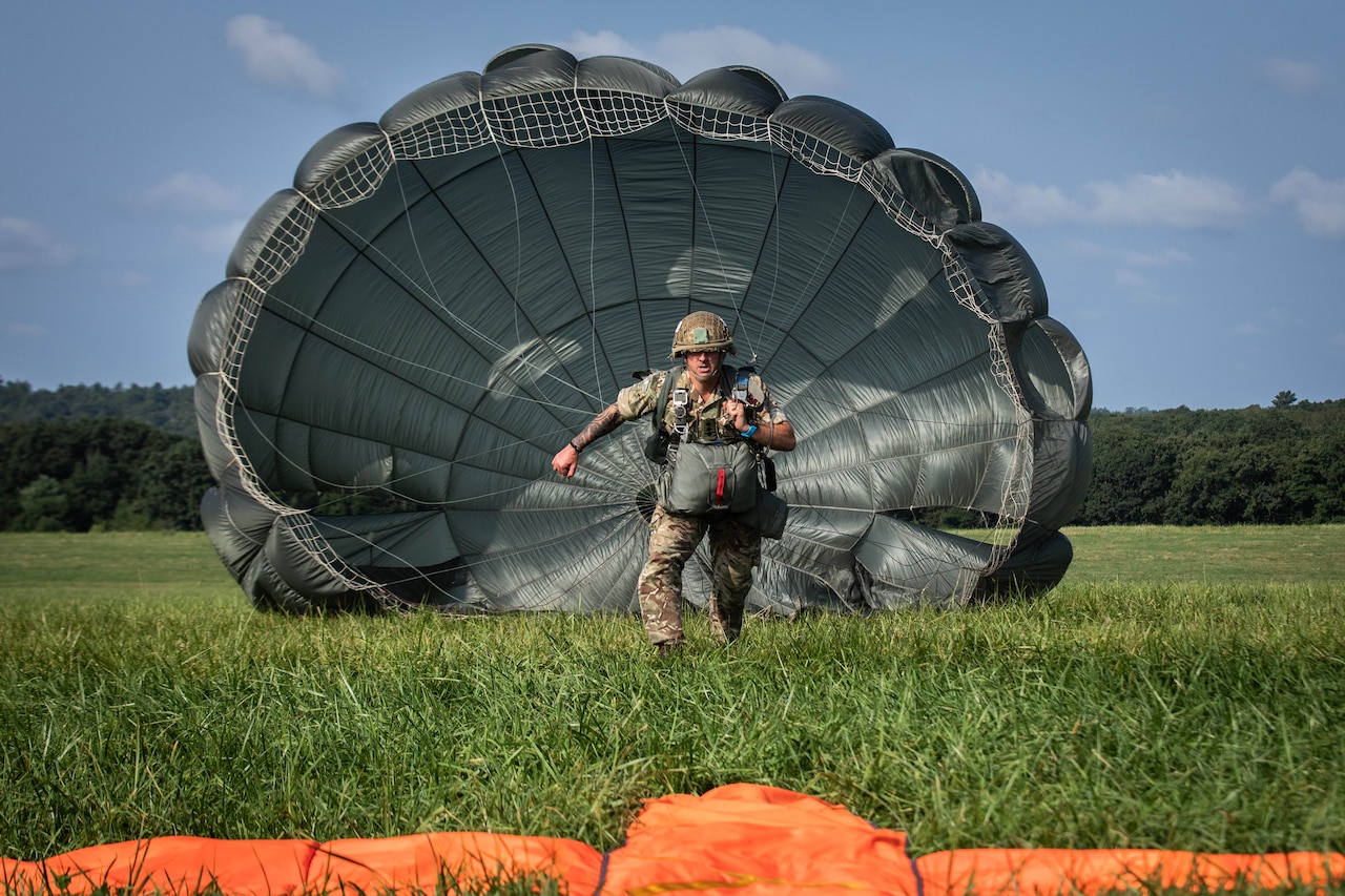 A paratrooper runs toward an orange target with his parachute behind him.