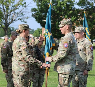 Male Soldier passes guidon to female soldier outside on Flagg Field during a change of command ceremony.