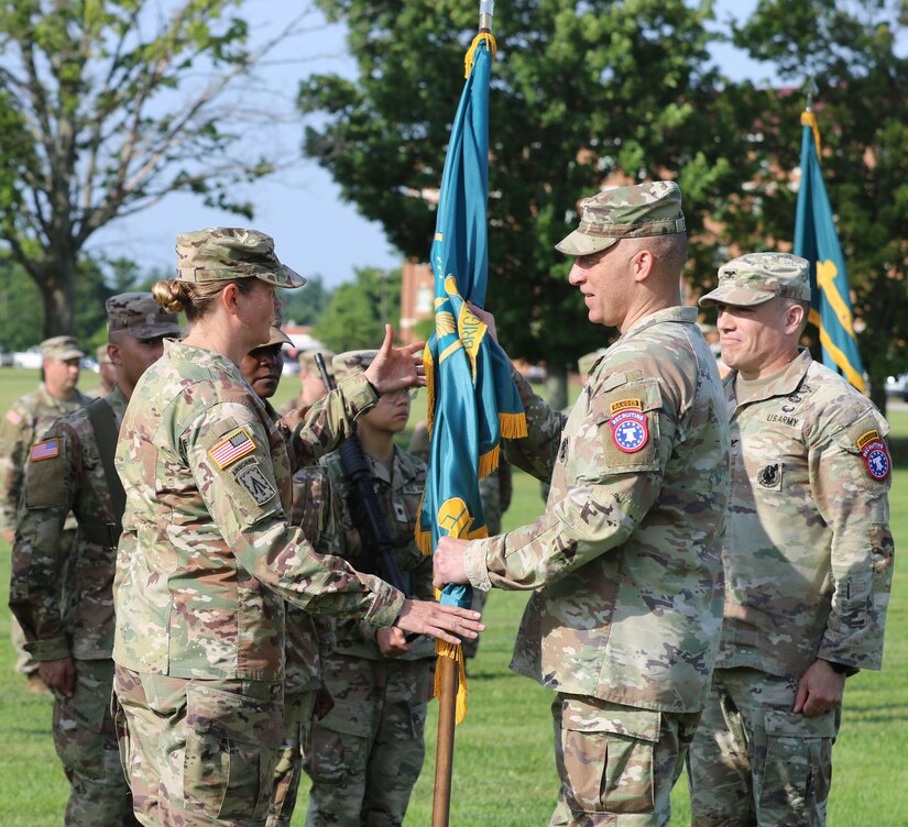 Male Soldier passes guidon to female soldier outside on Flagg Field during a change of command ceremony.