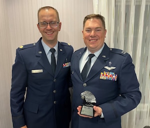 Two people in military service dress holding a trophy.