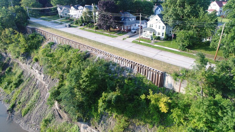 Overhead view of a shoreline stabilization project between a suburban residential roadway and an earthen slope to a river below.