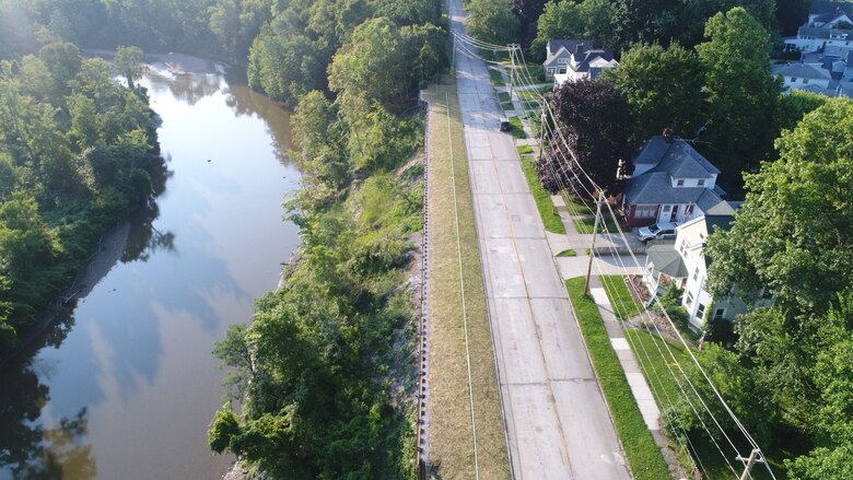 Overhead view of a shoreline stabilization project between a suburban residential roadway and an earthen slope to a river below.
