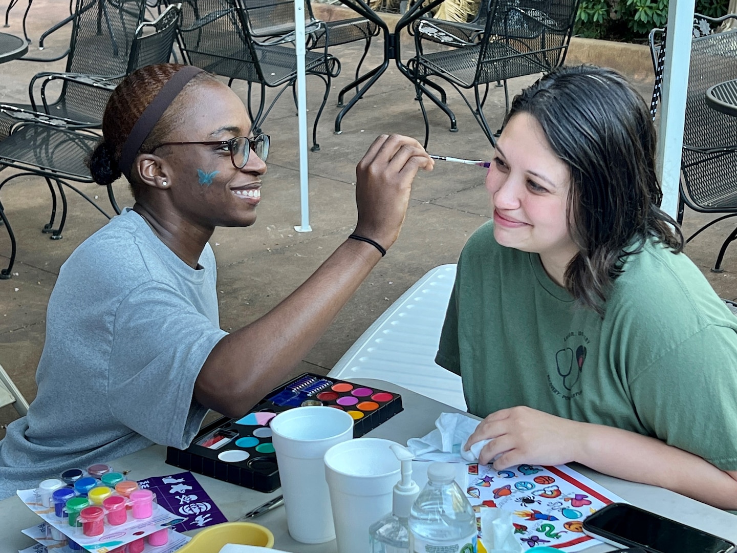 Woman getting her face painted by another woman.
