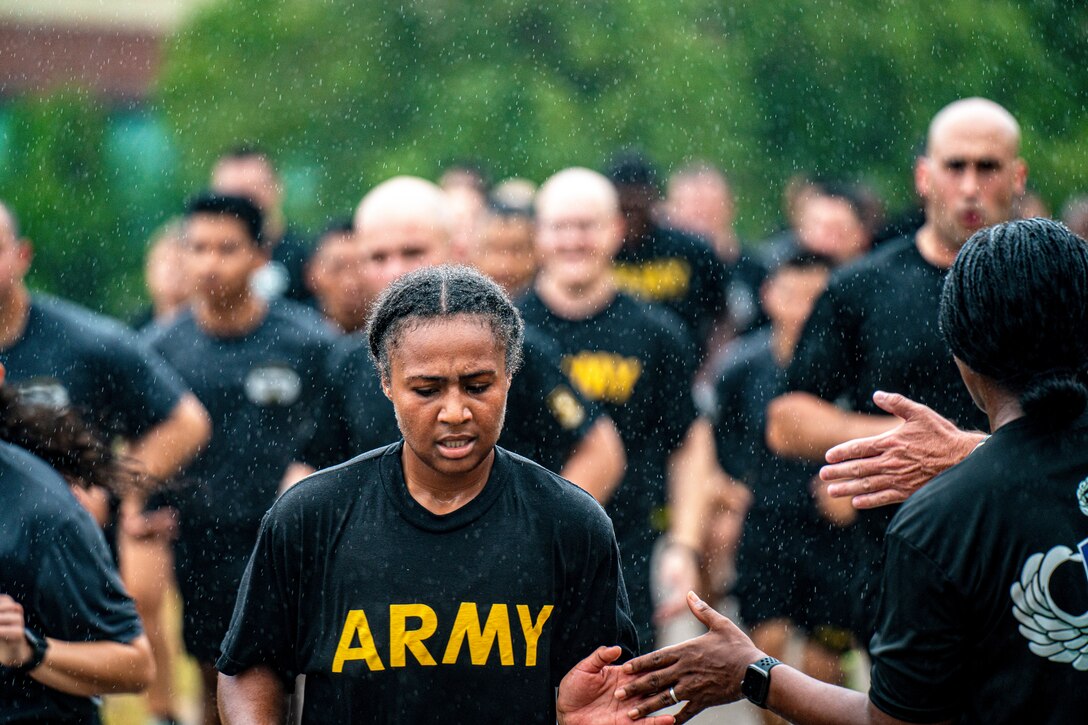 A soldier high-fives someone while running with fellow soldiers as it rains.