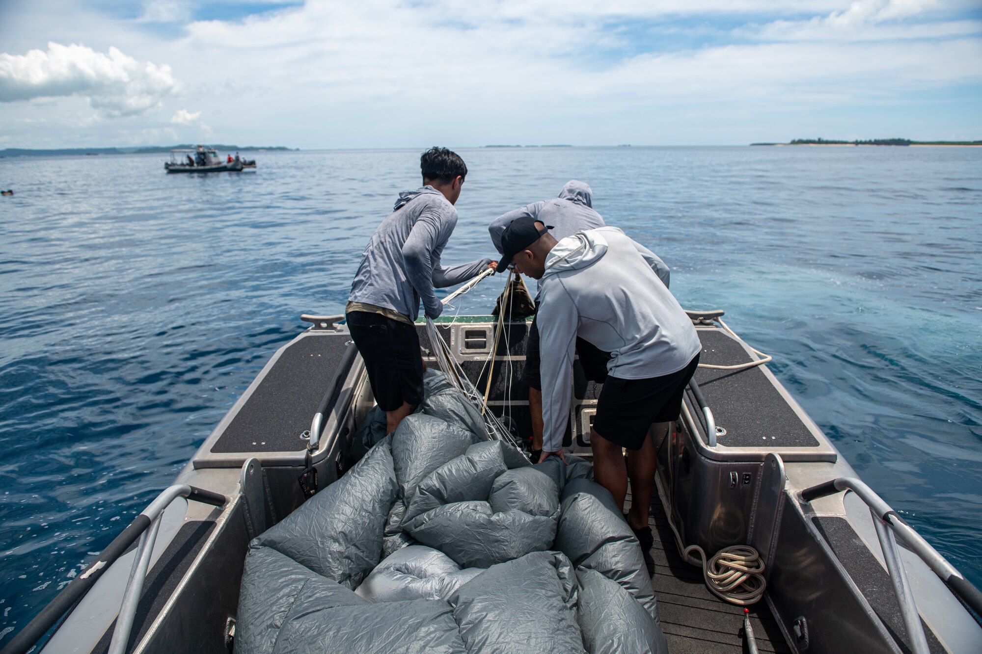 Three men pull a parachute from the water.