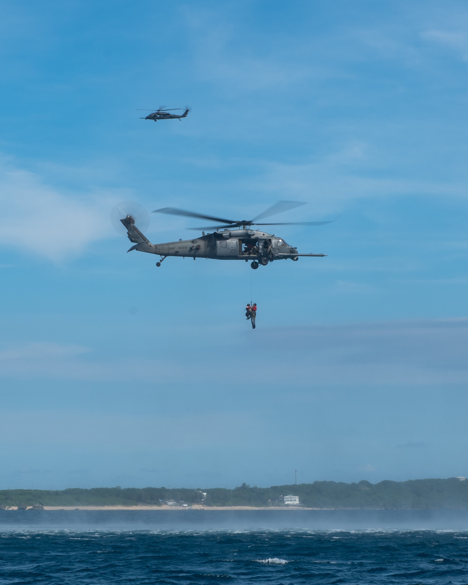 Two helicopters fly by people getting airlifted.