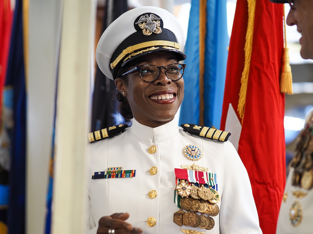 A Navy officer smiles in front of colorful flags