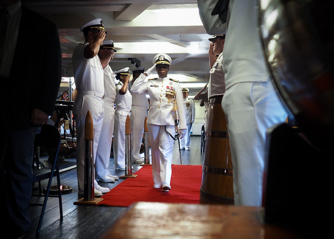 A Navy officer salutes as she walks between two rows of sailors
