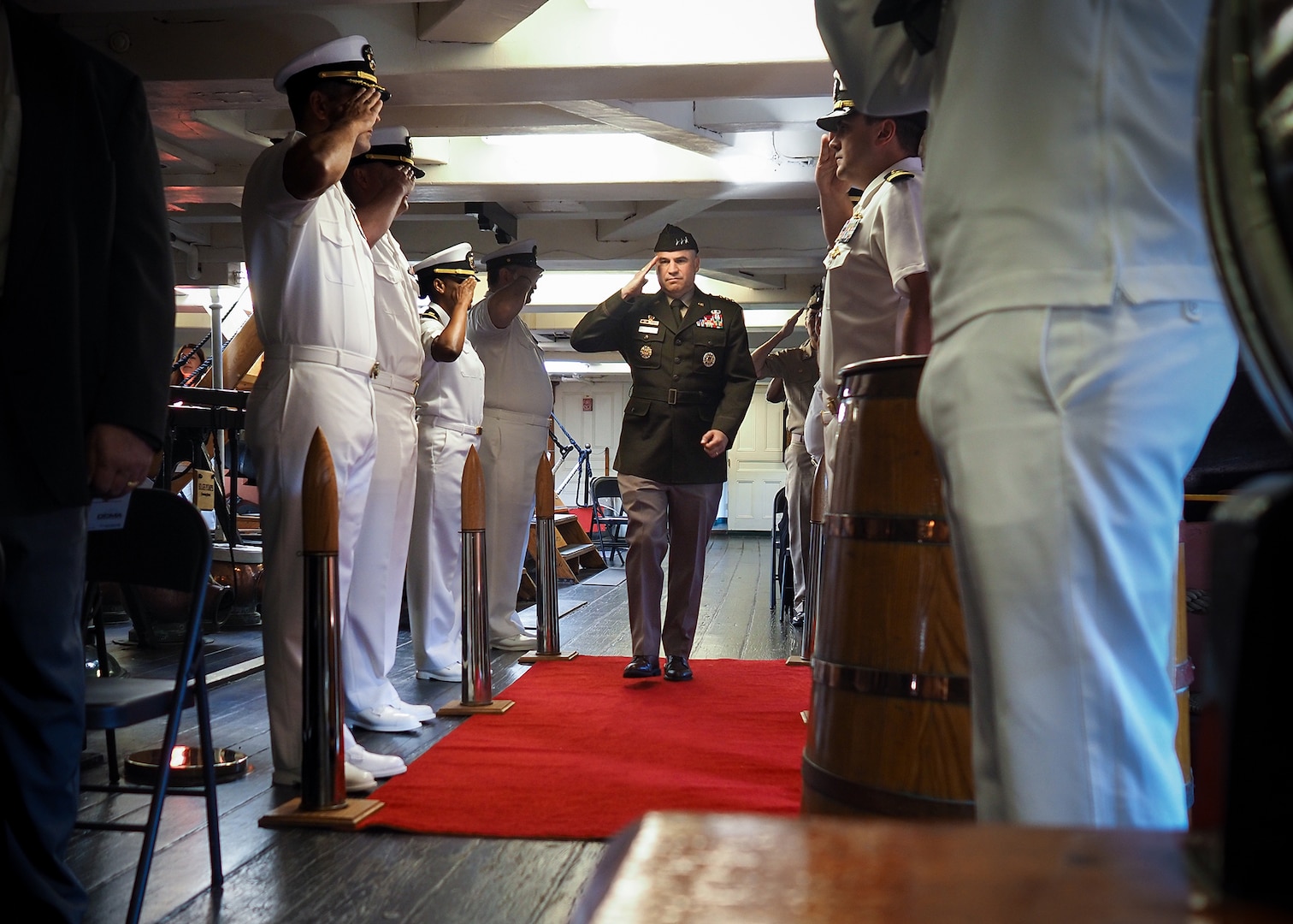 An Army officer salutes as he walks between two rows of sailors