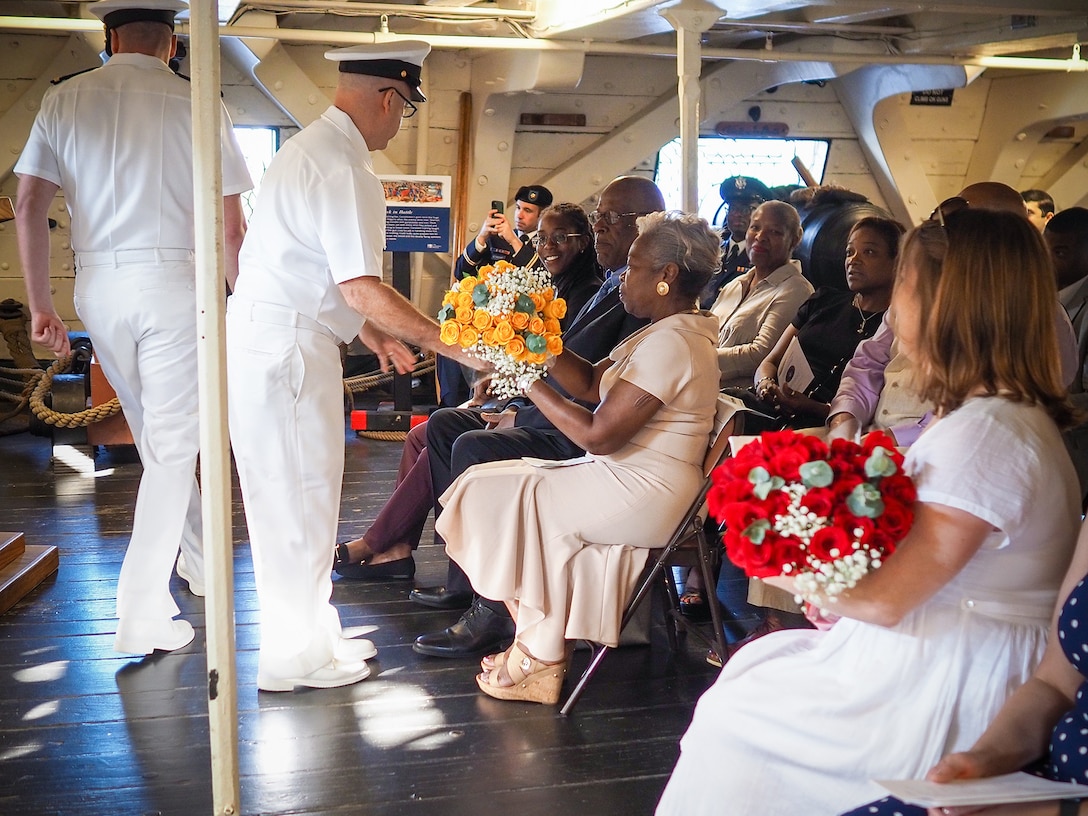 A Navy sailor hands flowers to a seated civilian woman