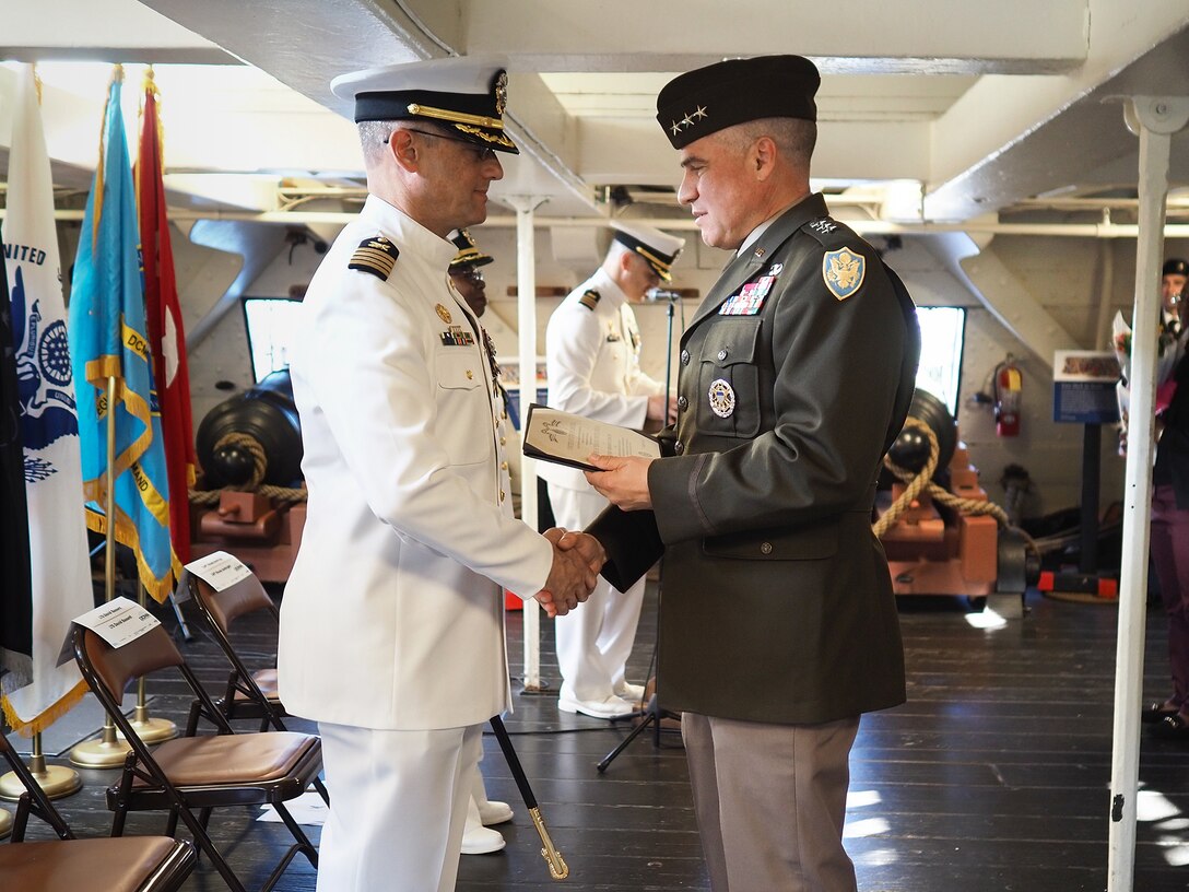 A Navy officer in white and an Army officer in green shake hands